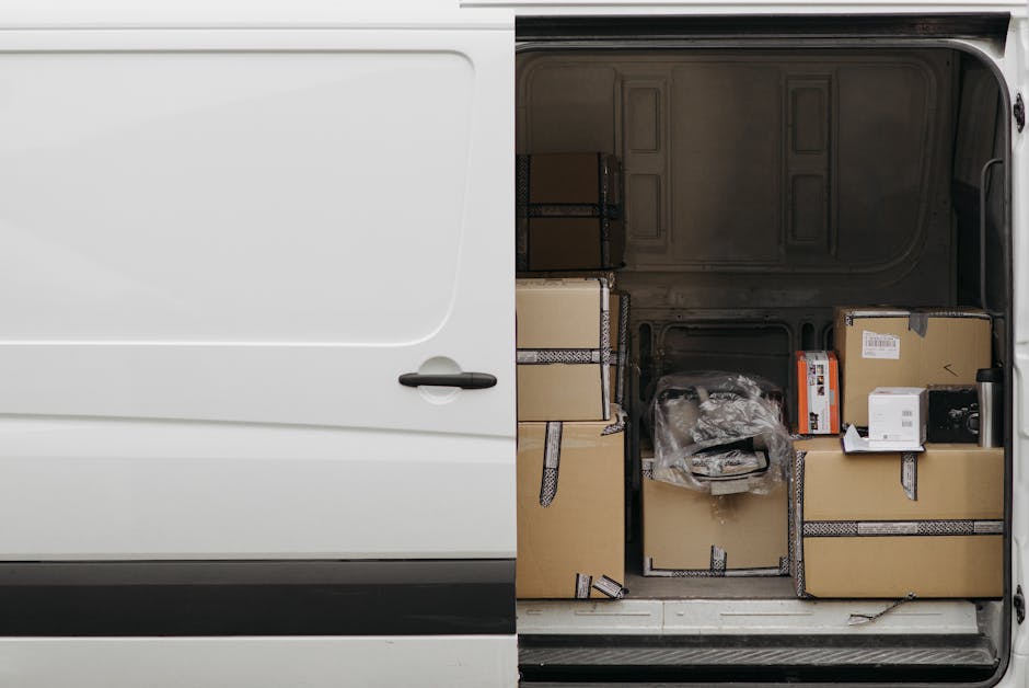 A vintage cream-coloured van with a compact, rounded shape, typical of older European utility vehicles, is shown in motion on a street, captured with a blurred background indicating speed. The van's cargo area is loaded with various household items, including wooden chairs, a table, and plastic and cardboard boxes, some wrapped in protective materials like fabric or plastic sheets. The furniture appears to be securely stacked and arranged to prevent movement during transit. The vehicle is part of a home relocation or furniture transport process associated with professional removals, possibly managed by company services such as Removal Companies Kennington. The scene depicts the loading or transportation phase in a moving service, highlighting the importance of careful packing and secure vehicle loading on a moving day, with an emphasis on efficiency and safety during the loading process.